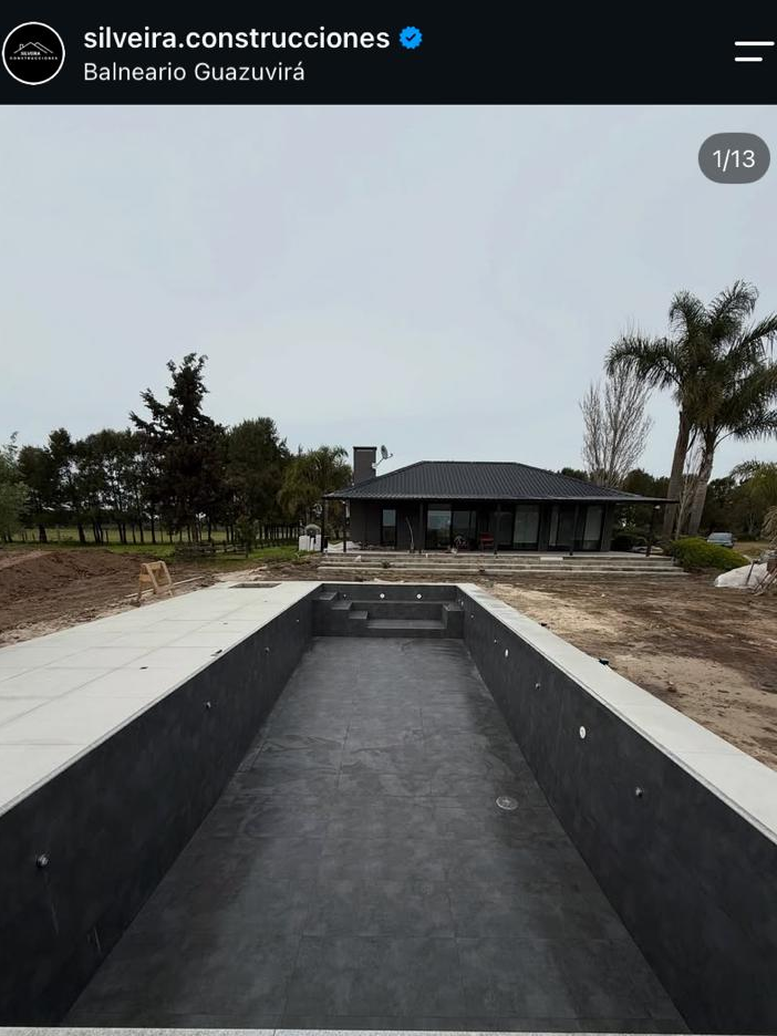 Captura de una publicación del Instagram de Silveira Construcciones: piscina vacía revestida en tonos oscuros en Balneario Guazuvirá, con una residencia al fondo.